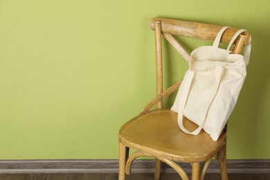 Photo of One eco bag on wooden chair near green wall. Mockup for design