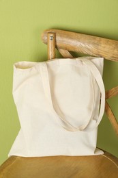 Photo of One eco bag on wooden chair near green wall. Mockup for design