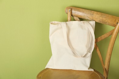 Photo of One eco bag on wooden chair near green wall. Mockup for design