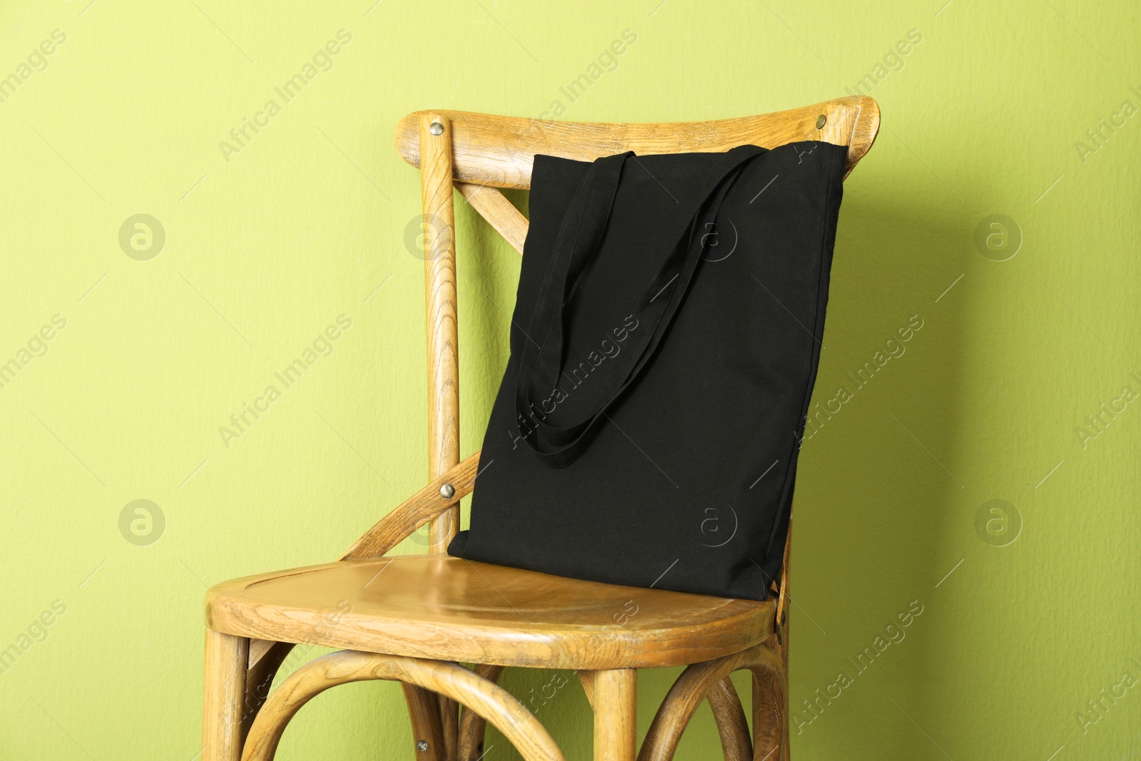 Photo of Black eco bag on wooden chair near green wall. Mockup for design