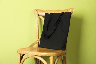 Photo of Black eco bag on wooden chair near green wall. Mockup for design