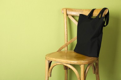 Photo of Black eco bag on wooden chair near green wall. Mockup for design