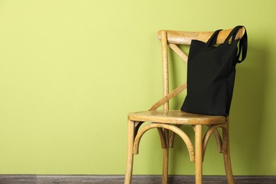 Photo of Black eco bag on wooden chair near green wall. Mockup for design