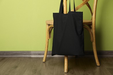 Photo of Black eco bag on wooden chair near green wall. Mockup for design