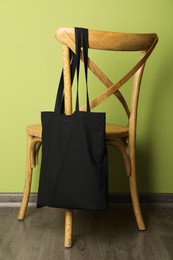 Photo of Black eco bag on wooden chair near green wall. Mockup for design