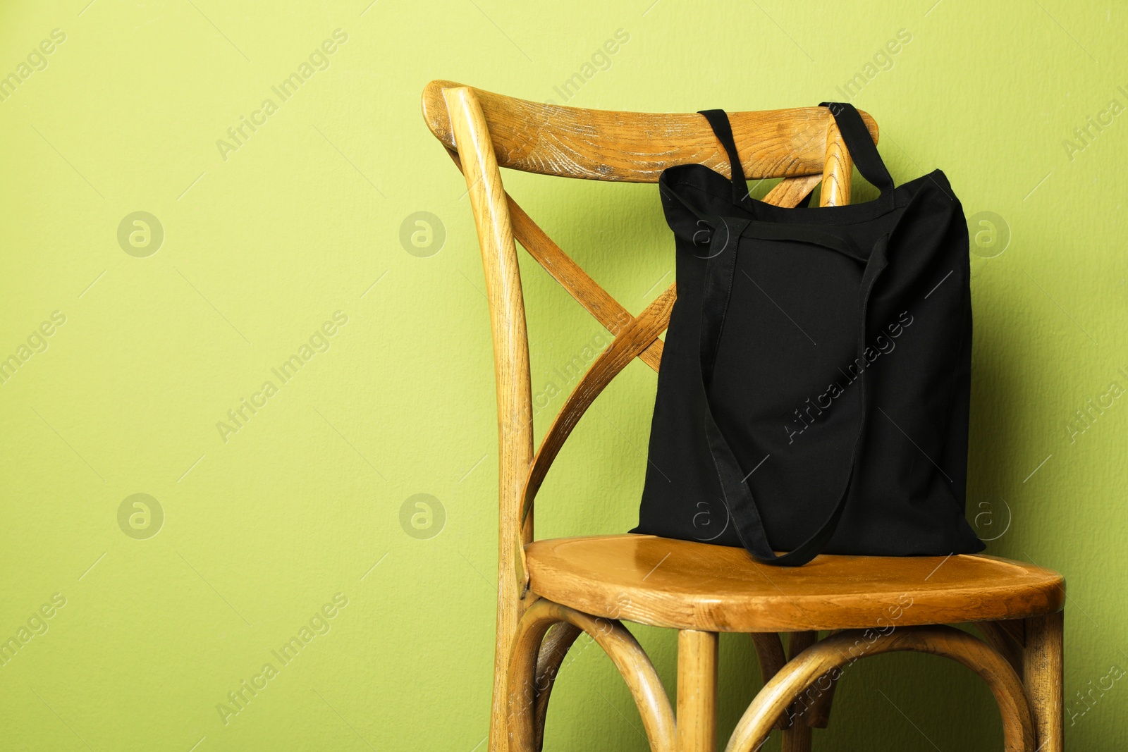 Photo of Black eco bag on wooden chair near green wall. Mockup for design