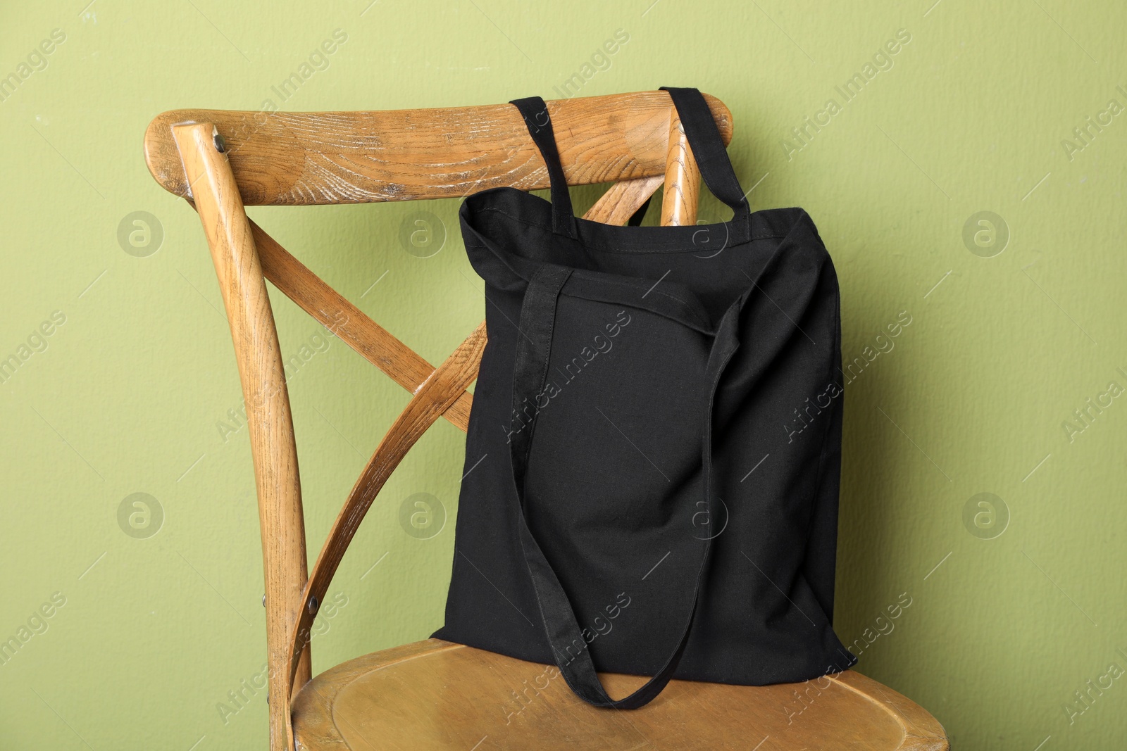 Photo of Black eco bag on wooden chair near green wall. Mockup for design