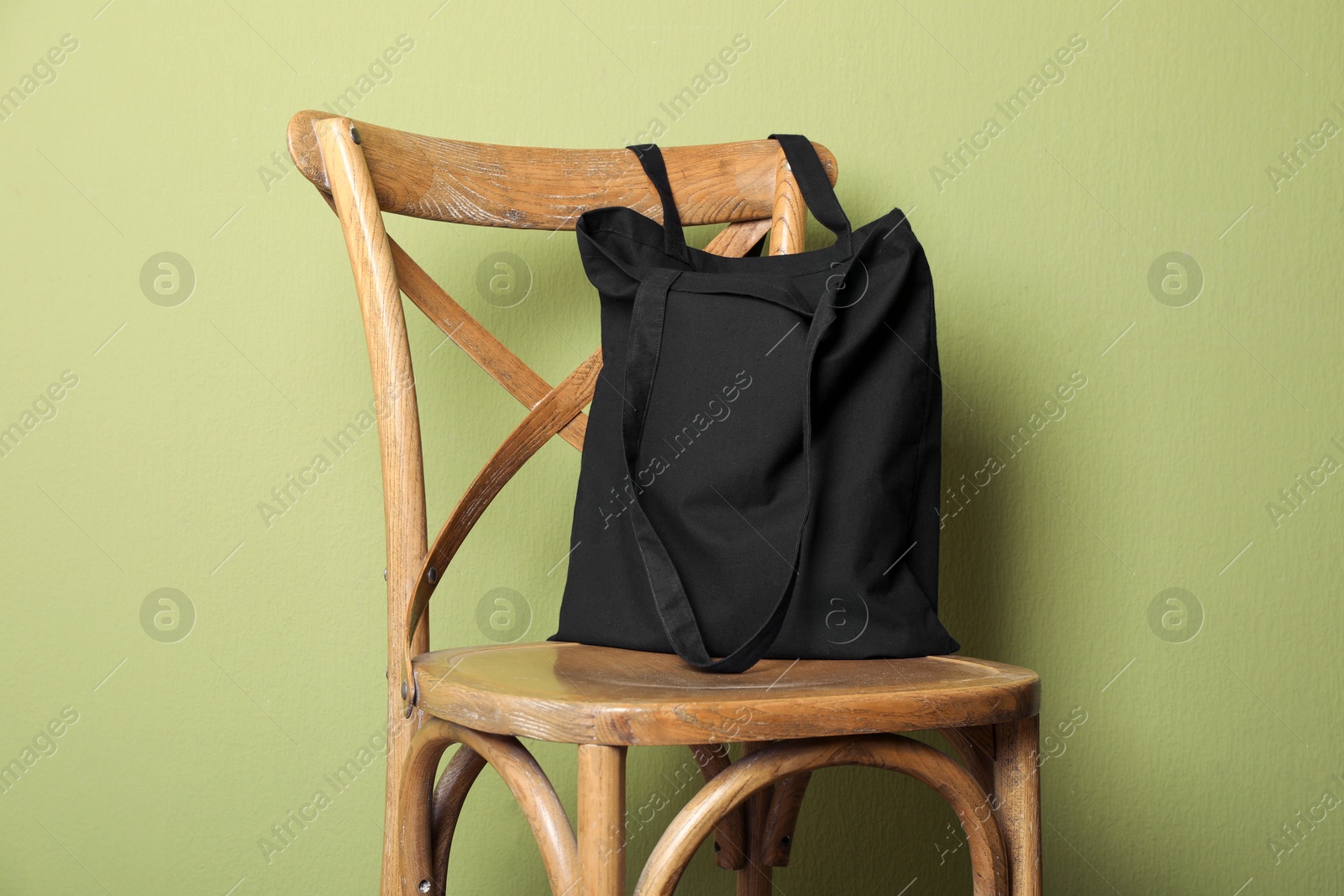 Photo of Black eco bag on wooden chair near green wall. Mockup for design