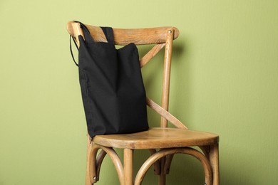 Photo of Black eco bag on wooden chair near green wall. Mockup for design