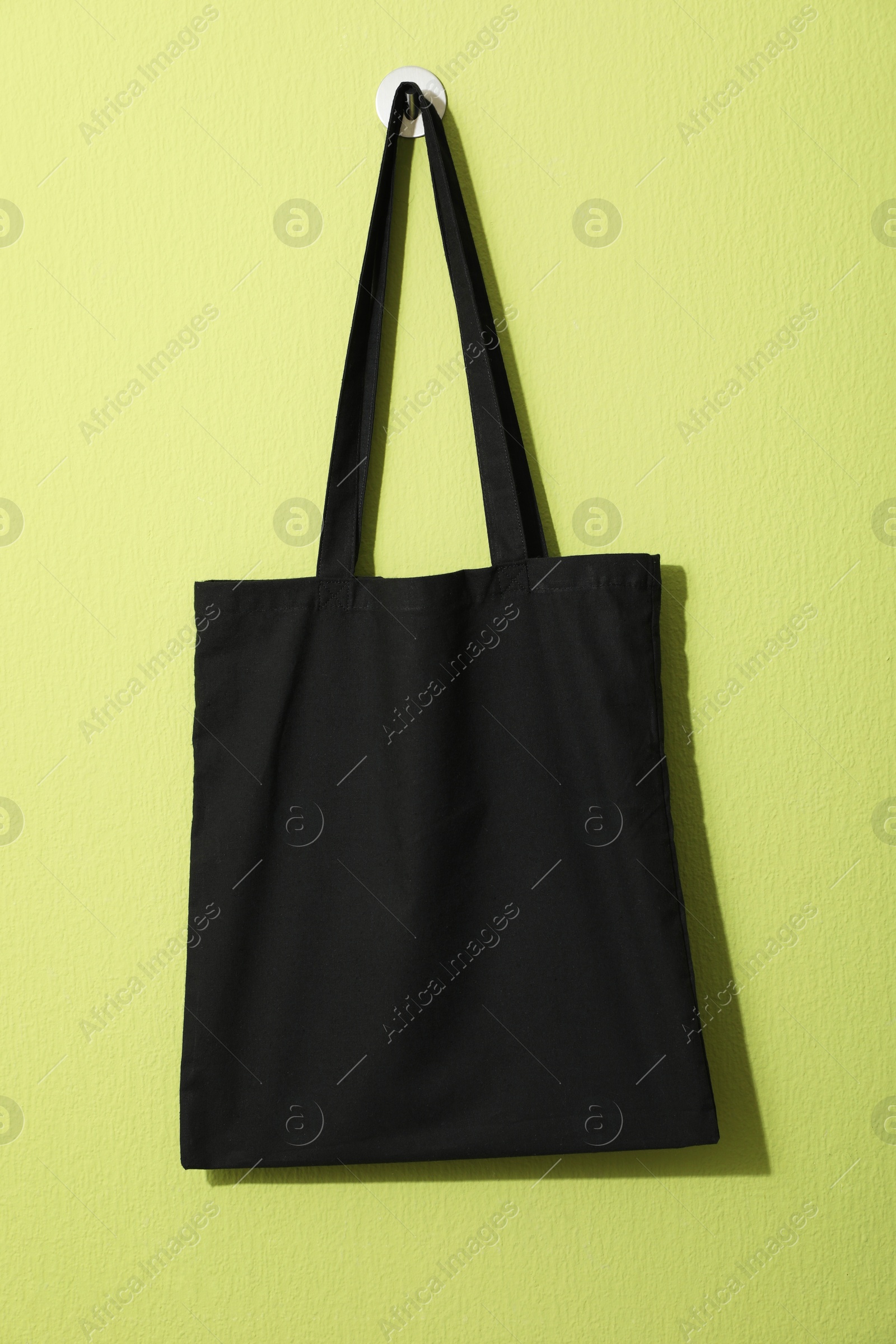 Photo of Black eco bag hanging on green wall. Mockup for design