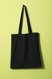 Photo of Black eco bag hanging on green wall. Mockup for design