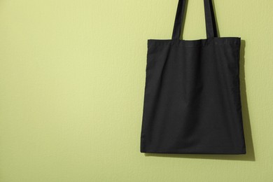 Photo of Black eco bag hanging on green wall. Mockup for design