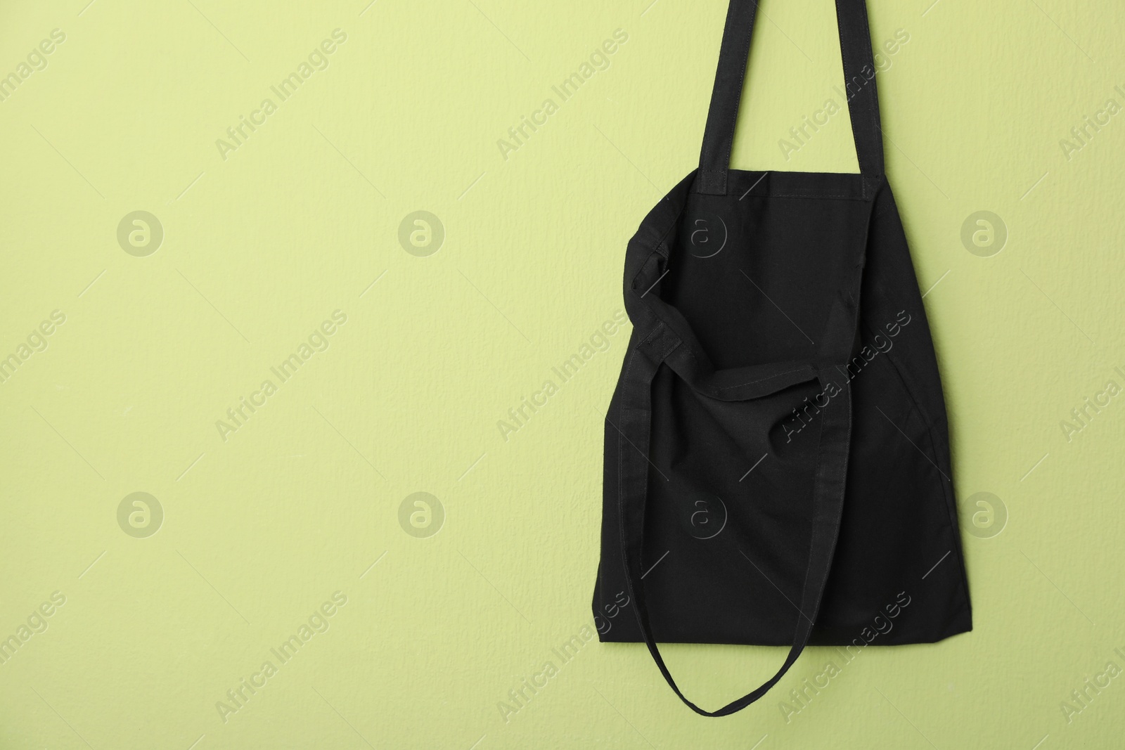 Photo of Black eco bag hanging on green wall. Mockup for design