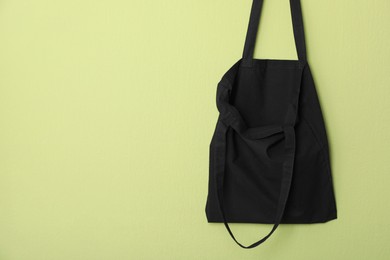 Photo of Black eco bag hanging on green wall. Mockup for design