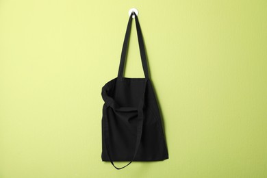 Photo of Black eco bag hanging on green wall. Mockup for design