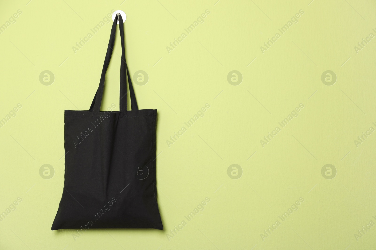 Photo of Black eco bag hanging on green wall. Mockup for design