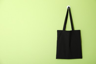 Photo of Black eco bag hanging on green wall. Mockup for design