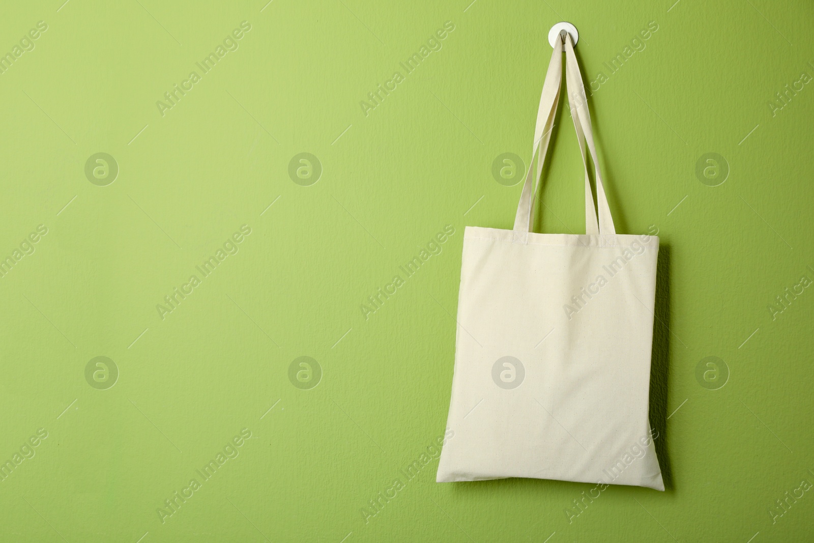 Photo of One eco bag hanging on green wall. Mockup for design