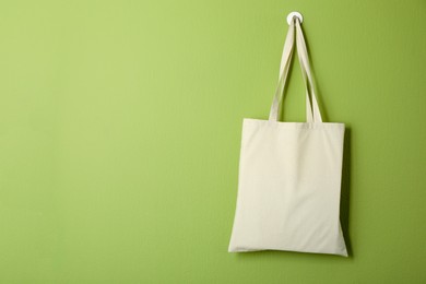 Photo of One eco bag hanging on green wall. Mockup for design