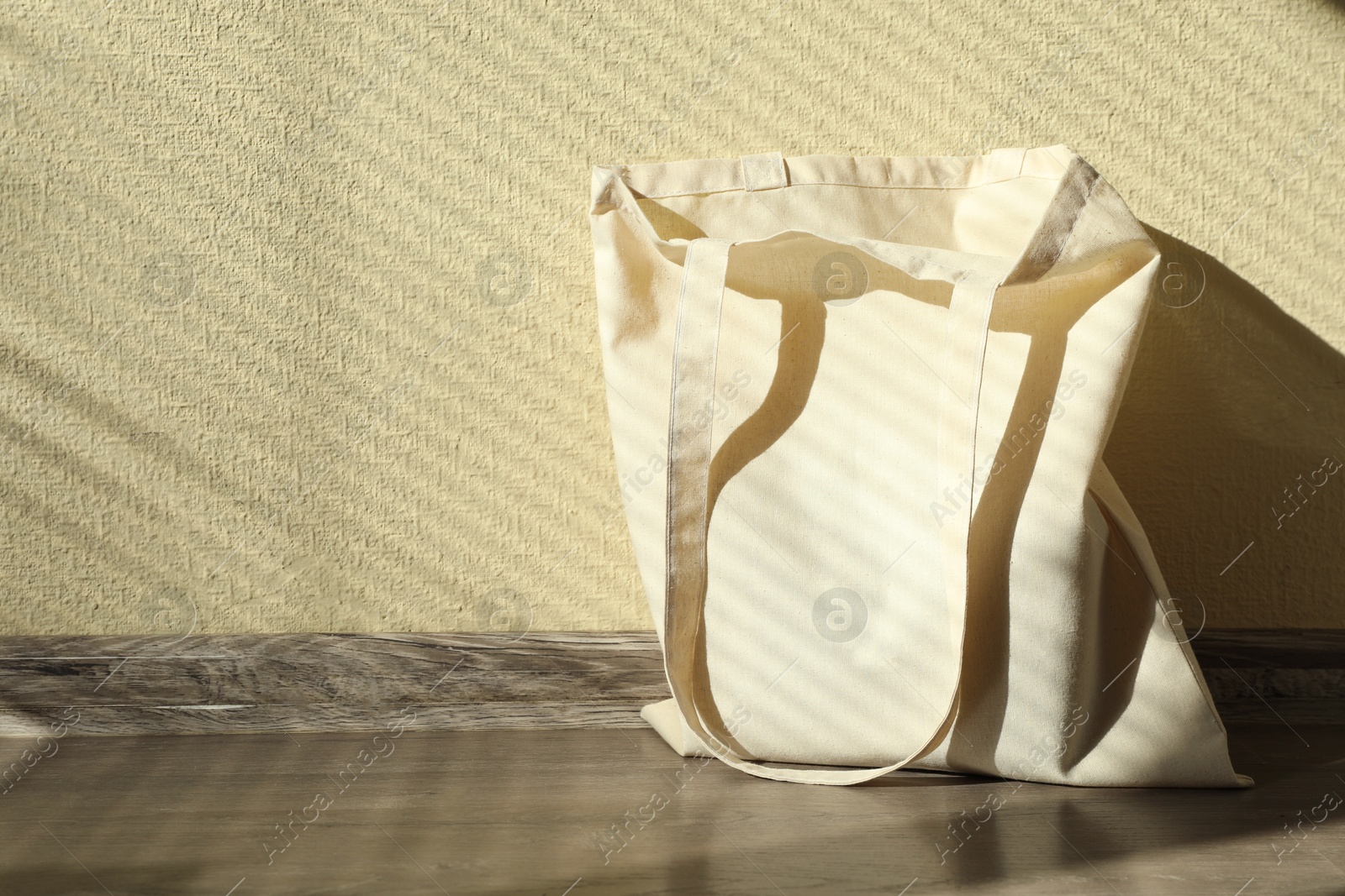 Photo of One eco bag on floor near beige wall. Mockup for design