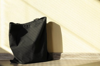 Photo of Black eco bag on floor near beige wall. Mockup for design