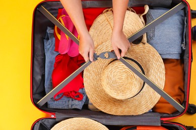 Photo of Traveler packing suitcase on yellow background, top view