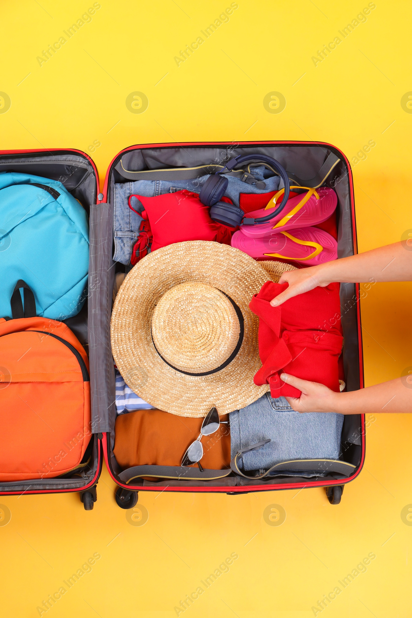 Photo of Traveler packing suitcase on yellow background, top view