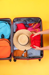 Photo of Traveler packing suitcase on yellow background, top view