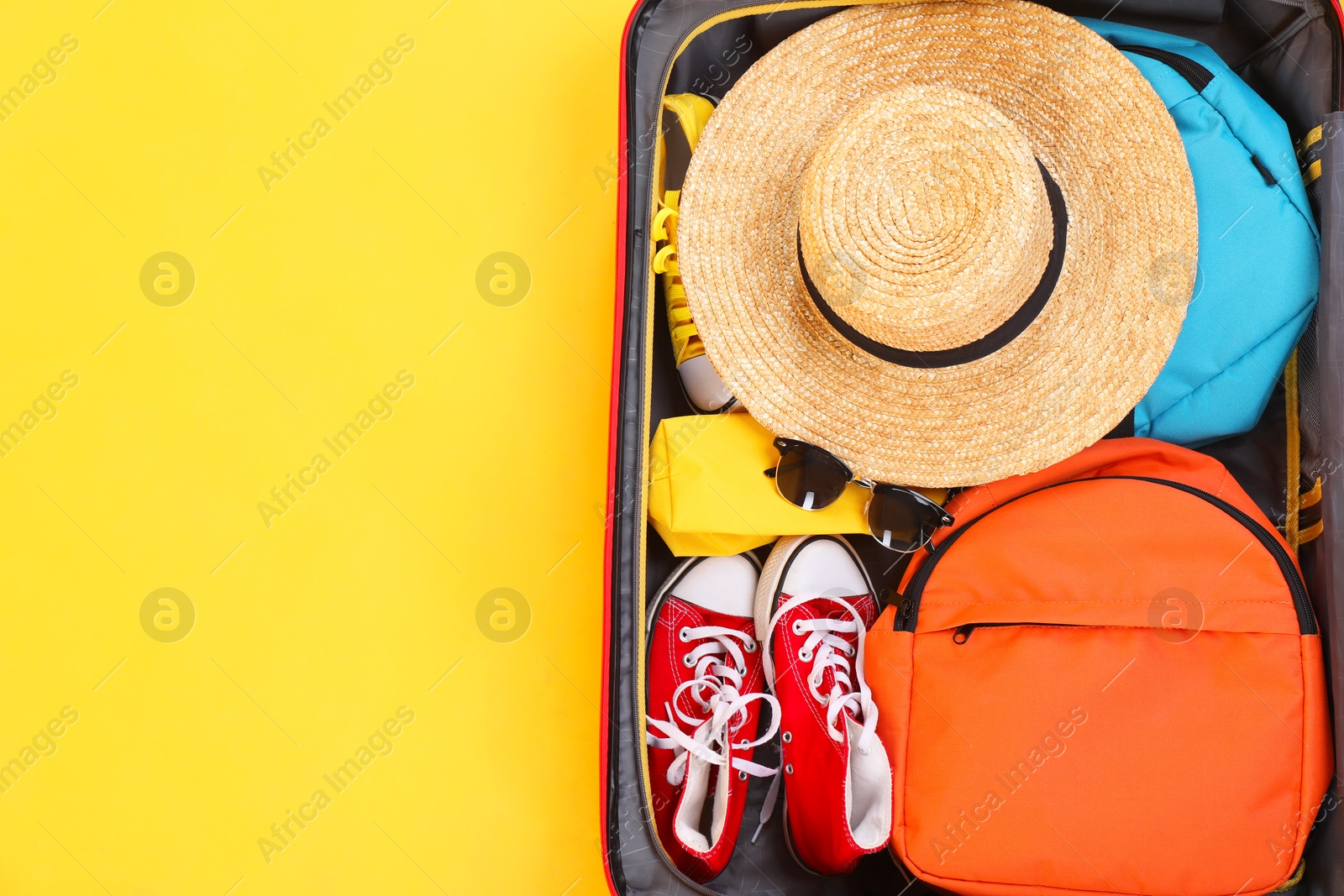 Photo of Travel abroad. Packed suitcase on yellow background, top view. Space for text