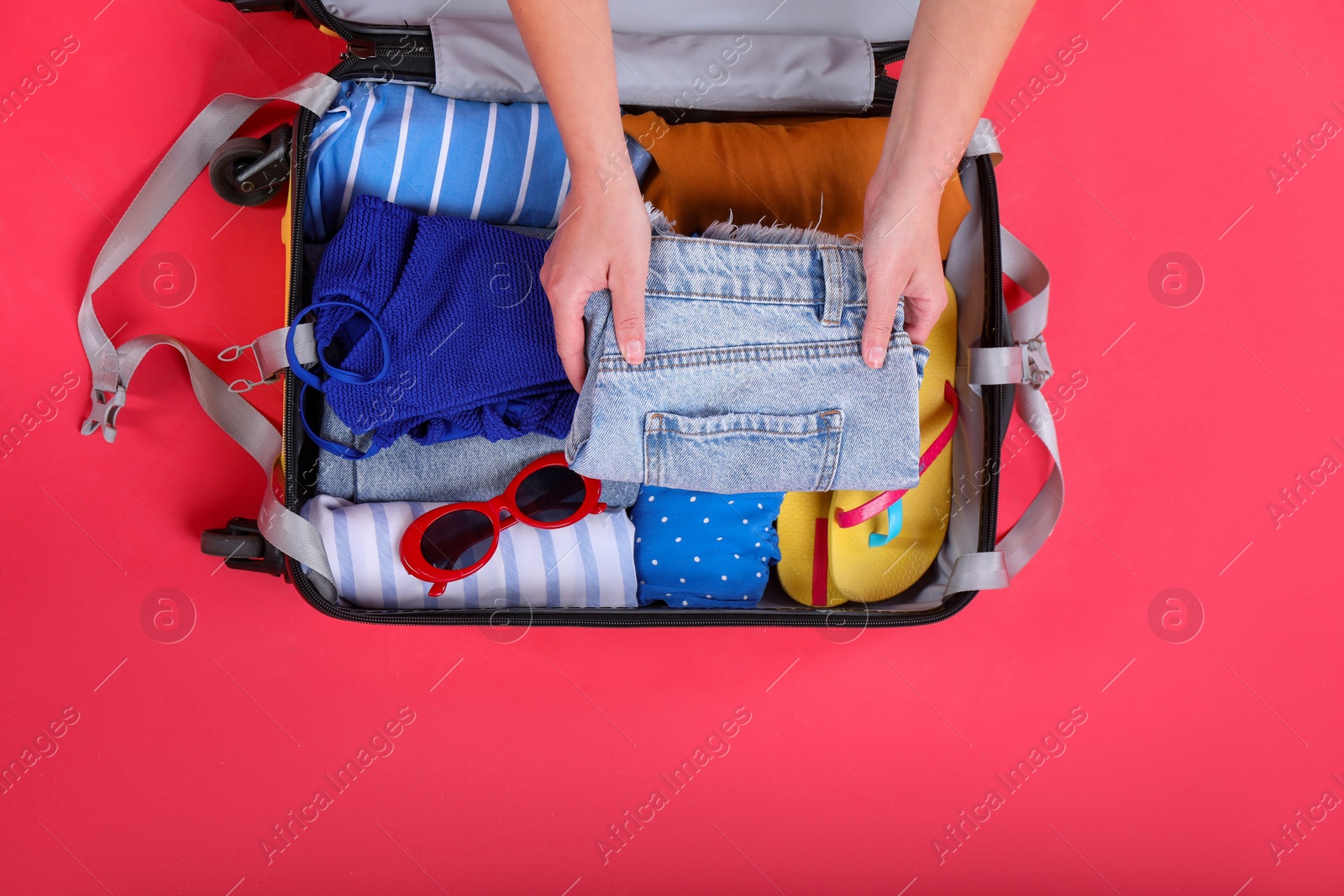 Photo of Traveler packing suitcase on red background, top view