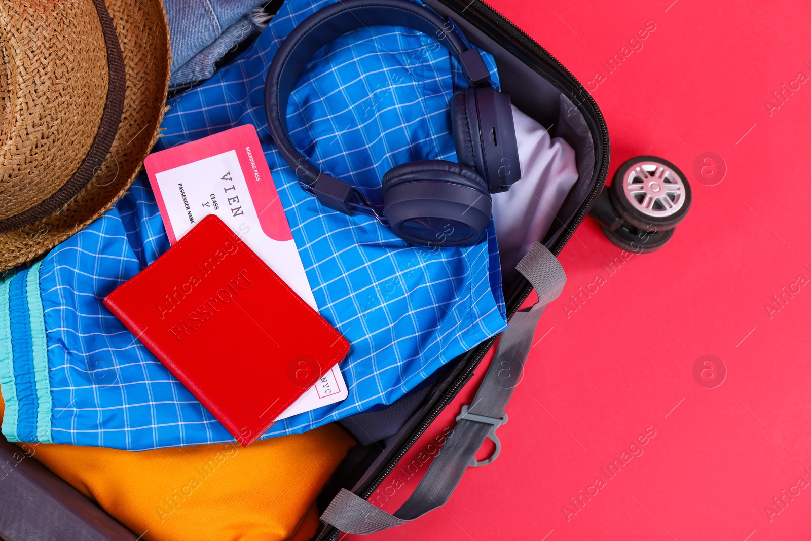 Photo of Travel abroad. Packed suitcase with passport and ticket on red background, closeup