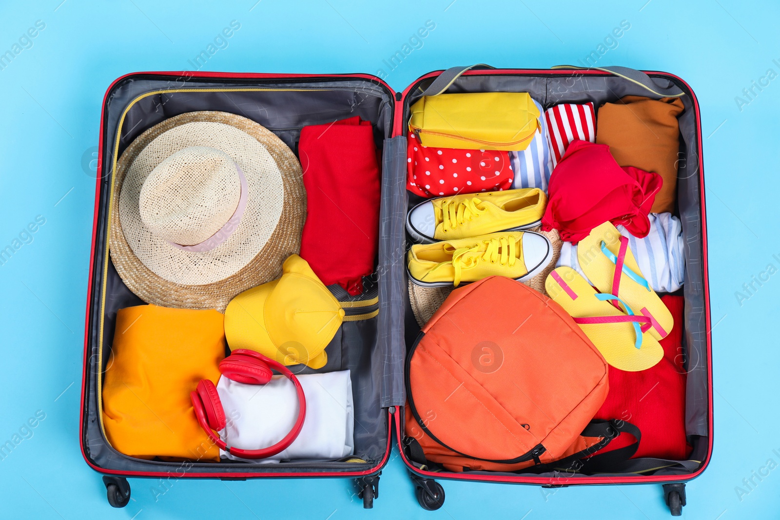 Photo of Travel abroad. Packed suitcase on light blue background, top view