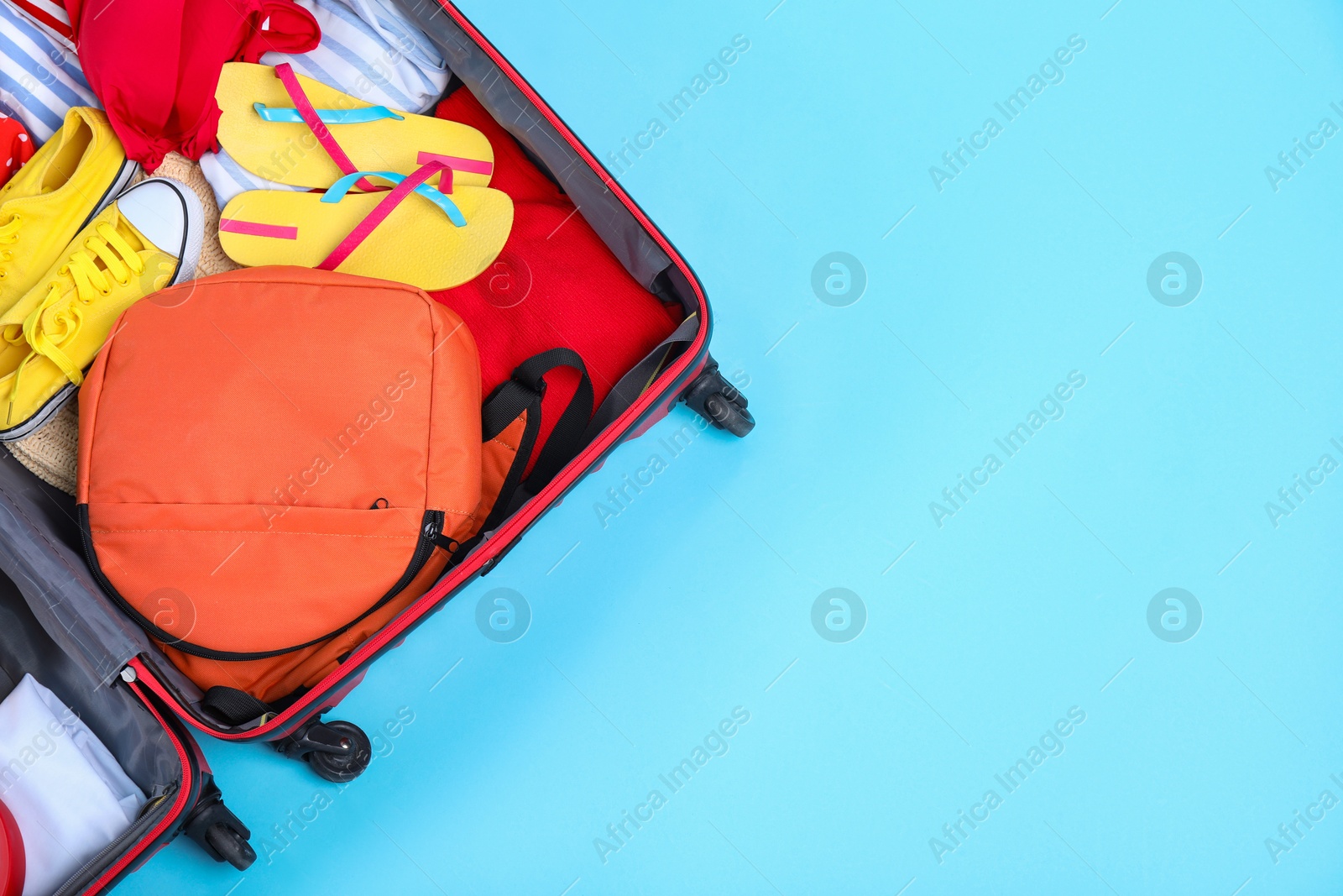 Photo of Travel abroad. Packed suitcase on light blue background, top view. Space for text