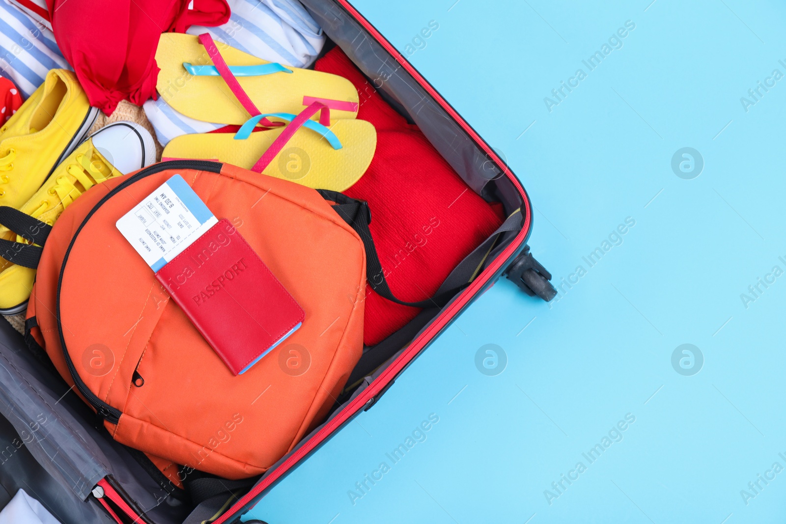 Photo of Travel abroad. Packed suitcase with passport and ticket on light blue background, top view