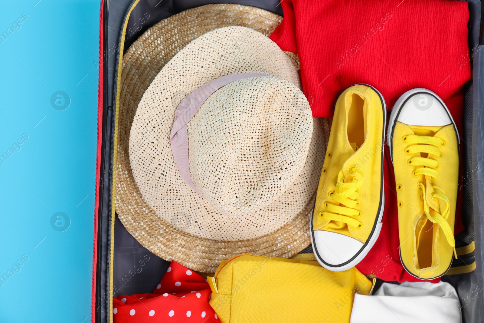 Photo of Travel abroad. Packed suitcase on light blue background, top view