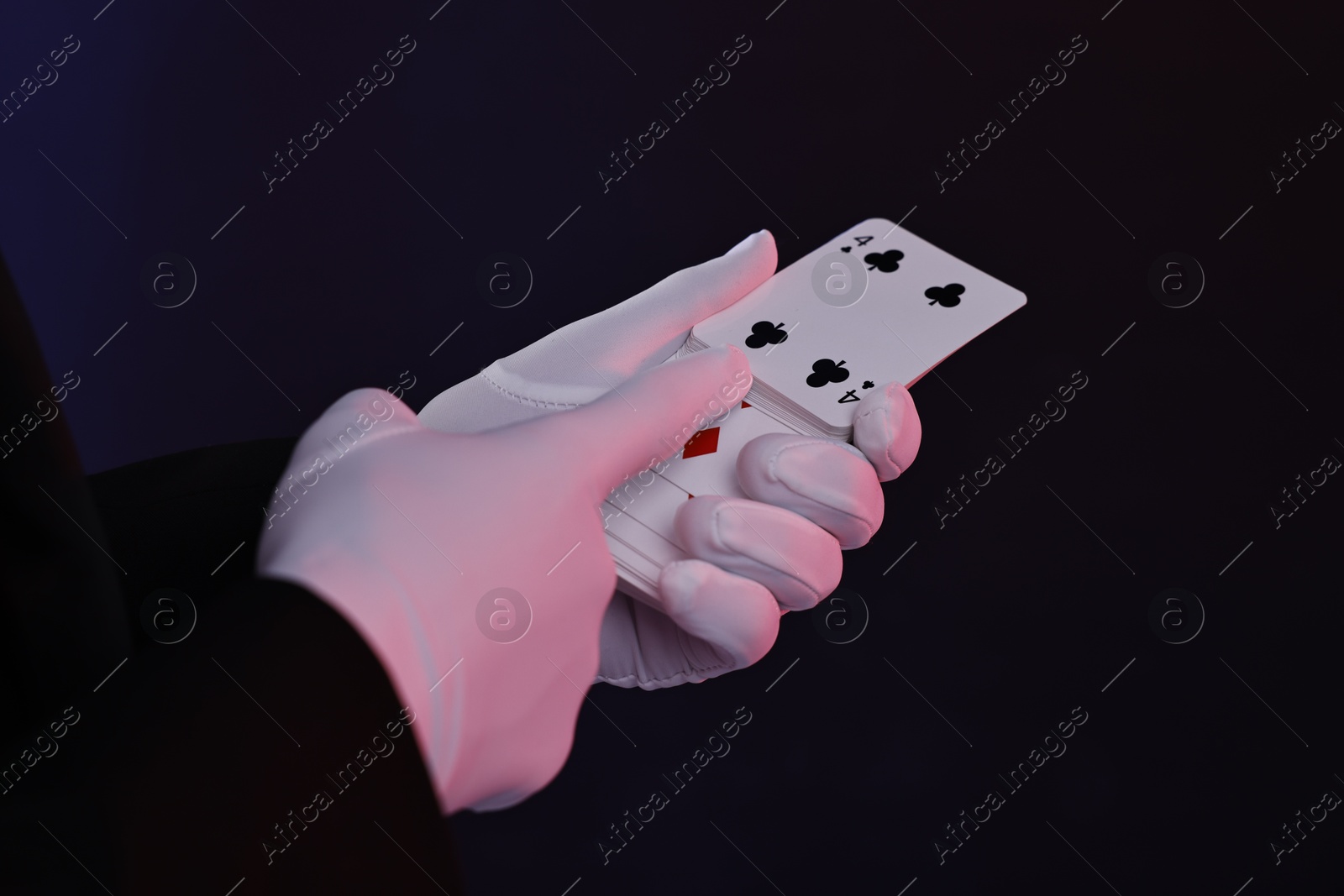 Photo of Illusionist with playing cards on dark background, closeup