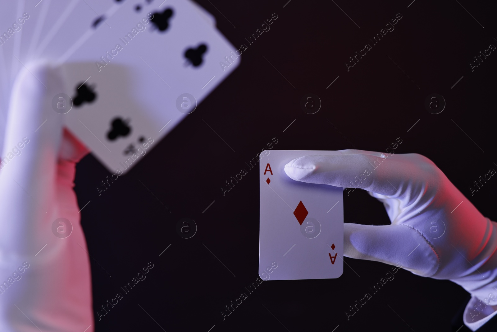 Photo of Illusionist with playing cards on dark background, closeup