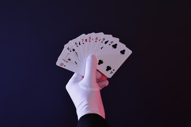 Photo of Illusionist with playing cards on dark background, closeup