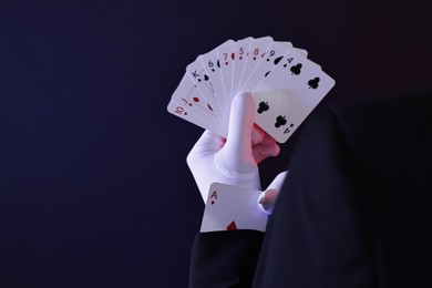 Photo of Illusionist hiding one playing card up his sleeve while showing deck on dark background, closeup. Space for text