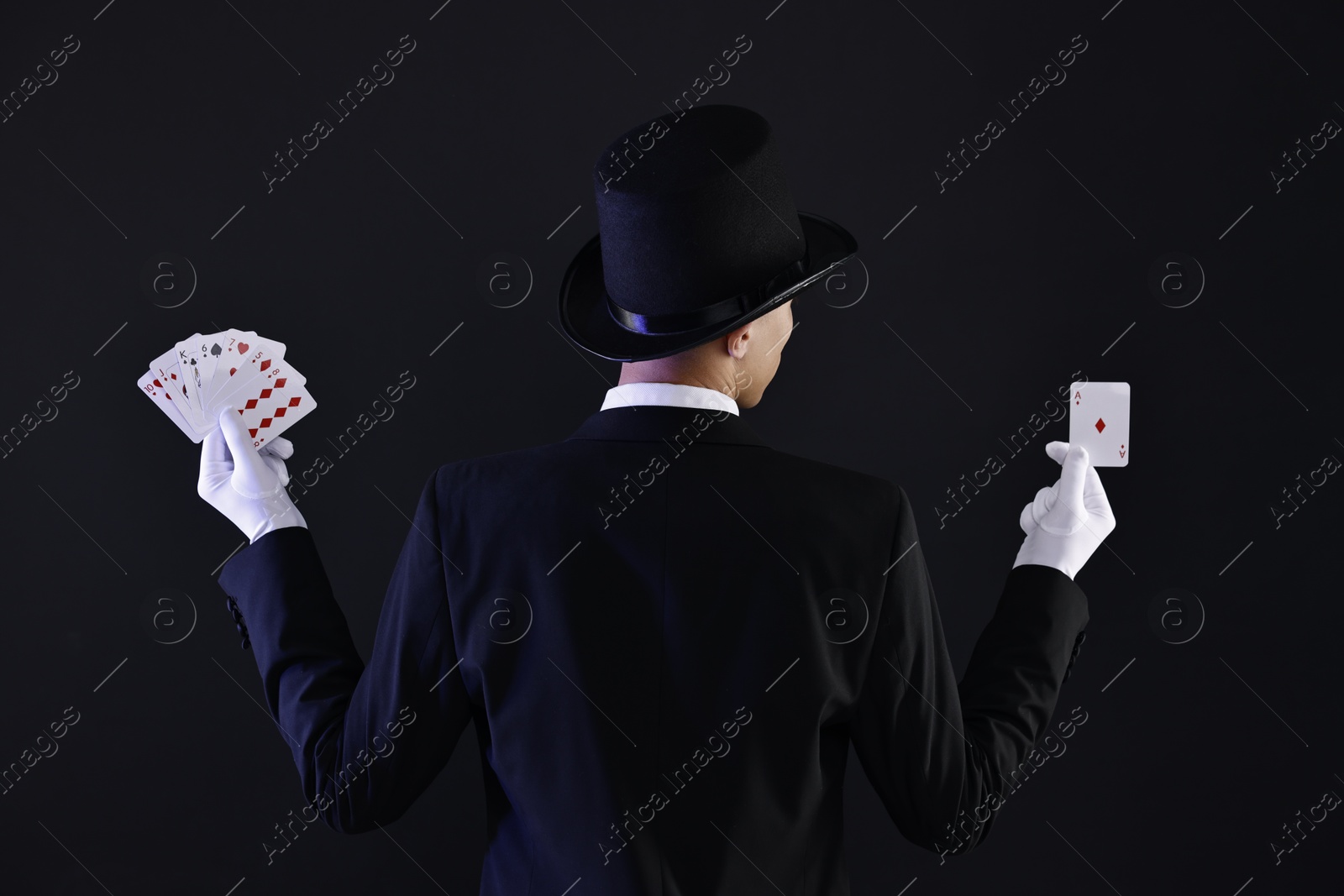 Photo of Illusionist with playing cards on black background, back view