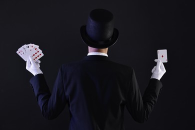 Photo of Illusionist with playing cards on black background, back view