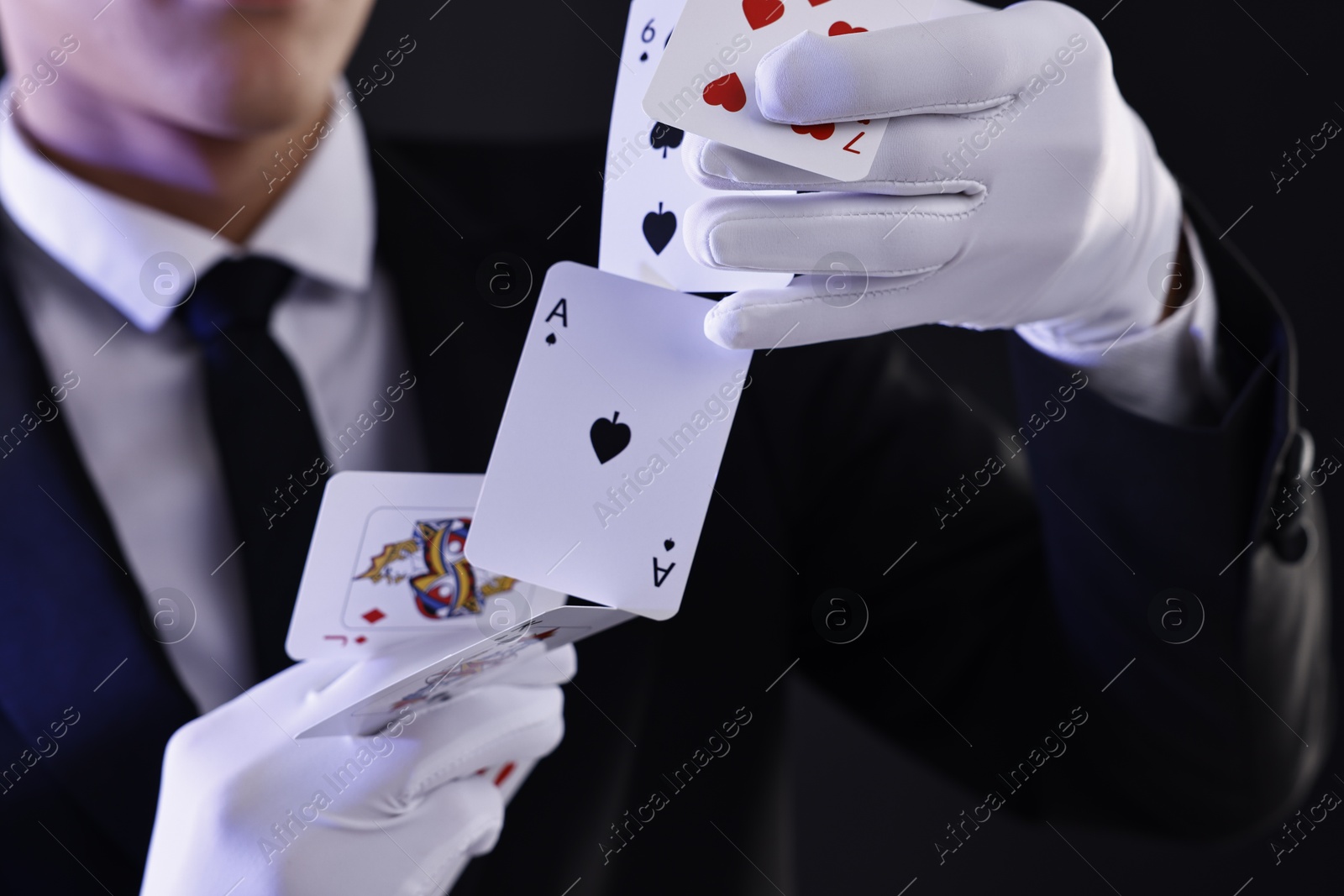 Photo of Illusionist showing trick with playing cards on black background, closeup