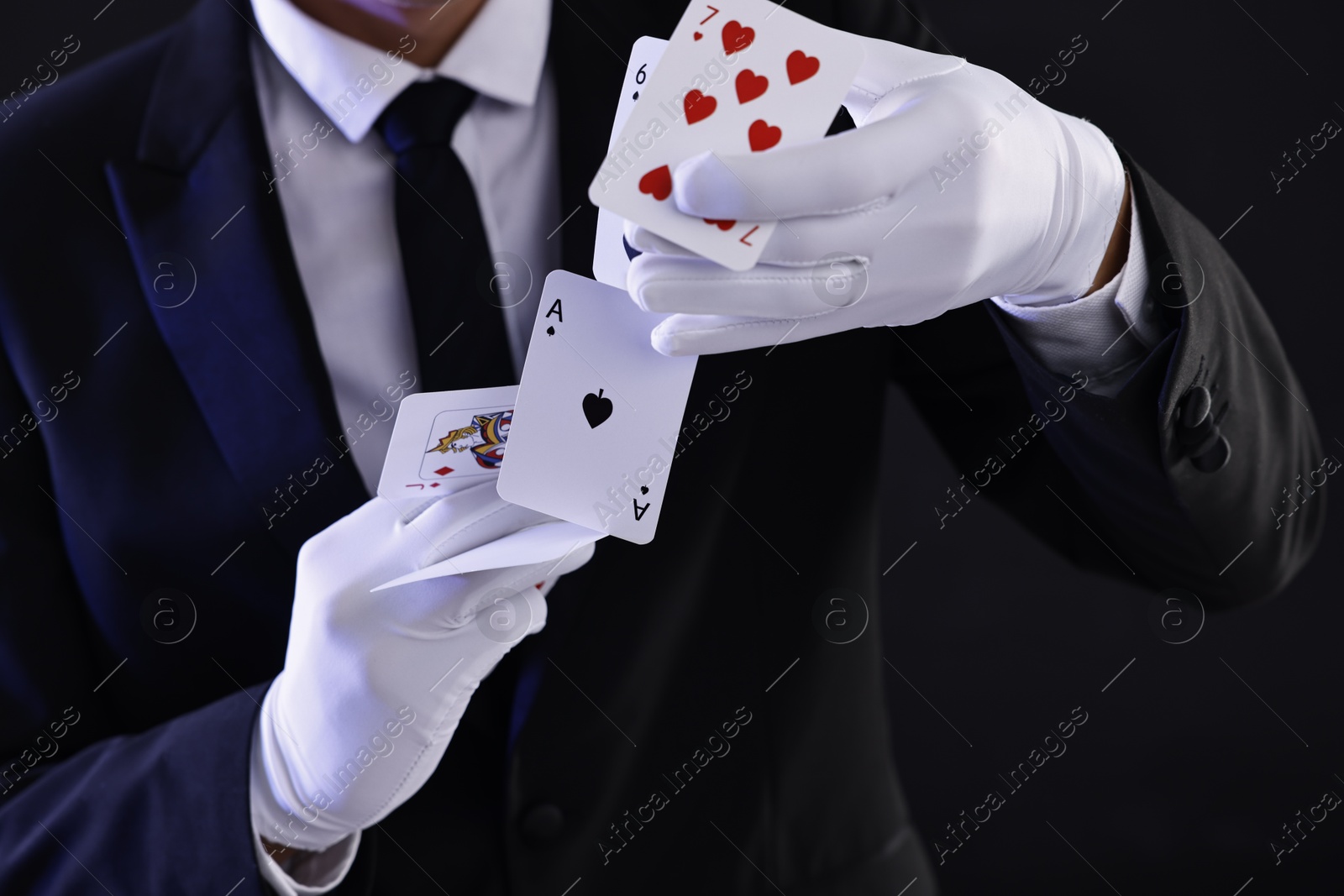 Photo of Illusionist showing trick with playing cards on black background, closeup