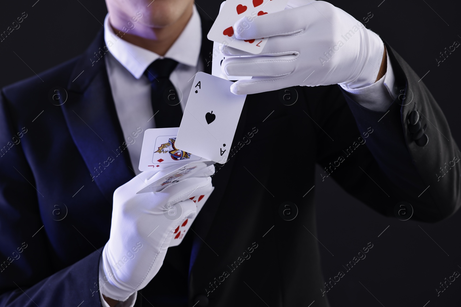 Photo of Illusionist showing trick with playing cards on black background, closeup