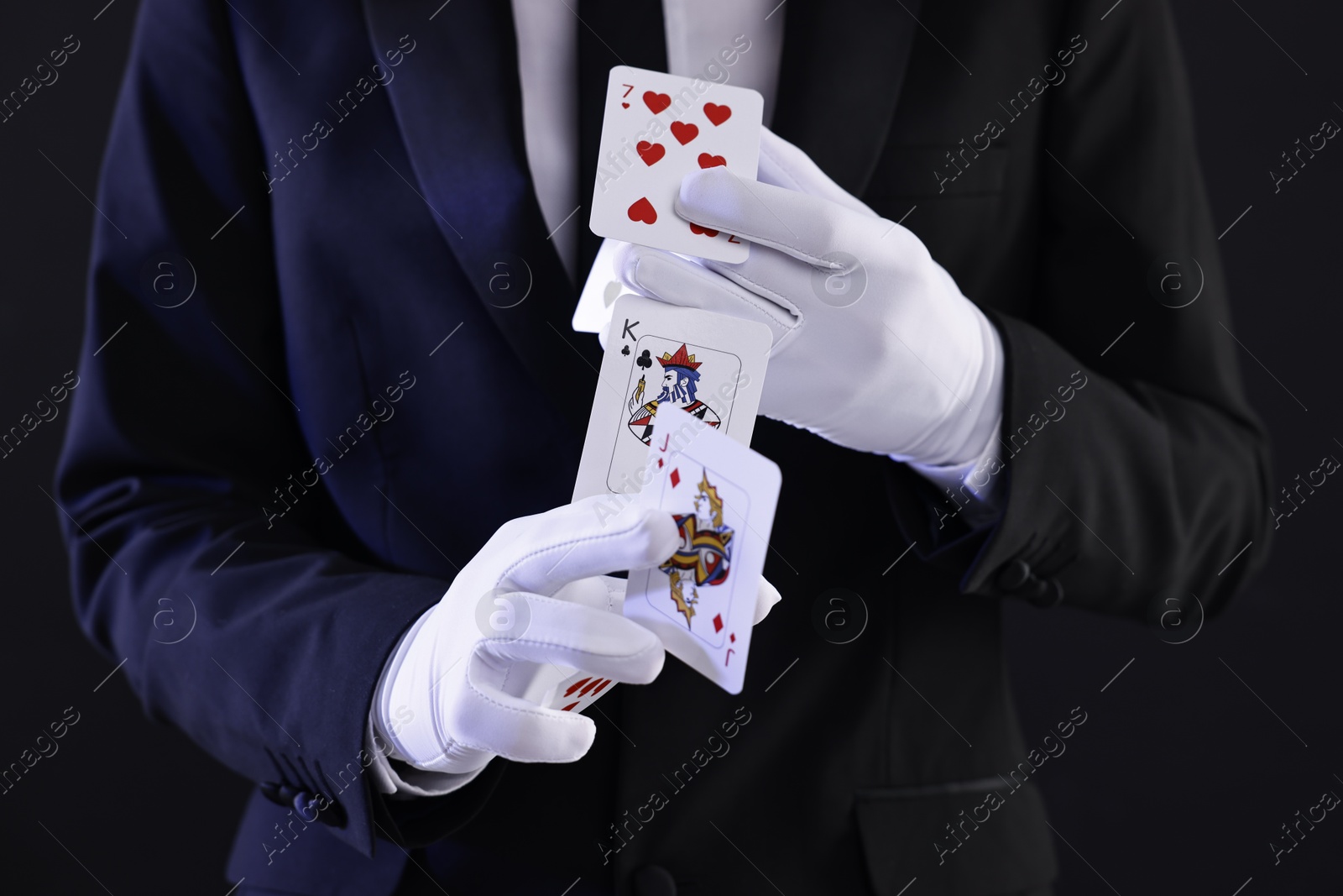 Photo of Illusionist showing trick with playing cards on black background, closeup