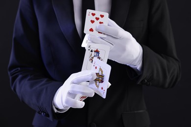 Photo of Illusionist showing trick with playing cards on black background, closeup