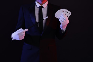 Photo of Illusionist pointing magic wand on playing cards against black background, closeup