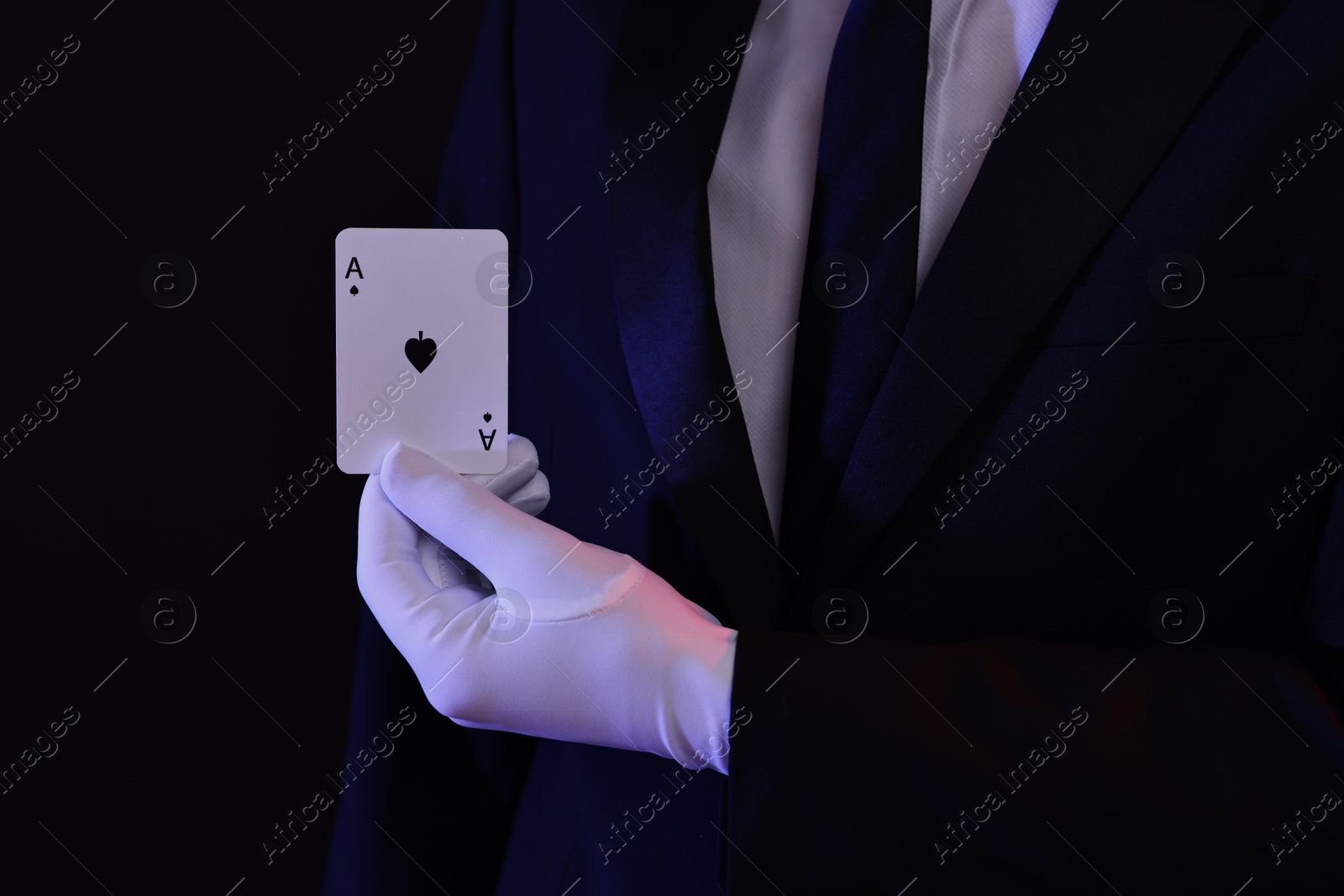 Photo of Illusionist showing playing card on black background, closeup