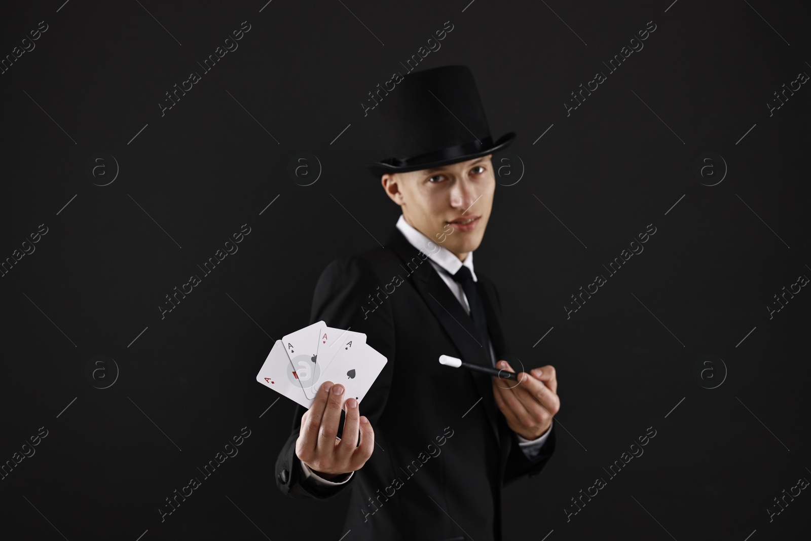 Photo of Illusionist pointing magic wand on playing cards against black background, selective focus