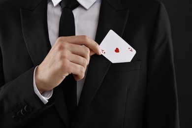 Photo of Illusionist taking playing card out of pocket on black background, closeup